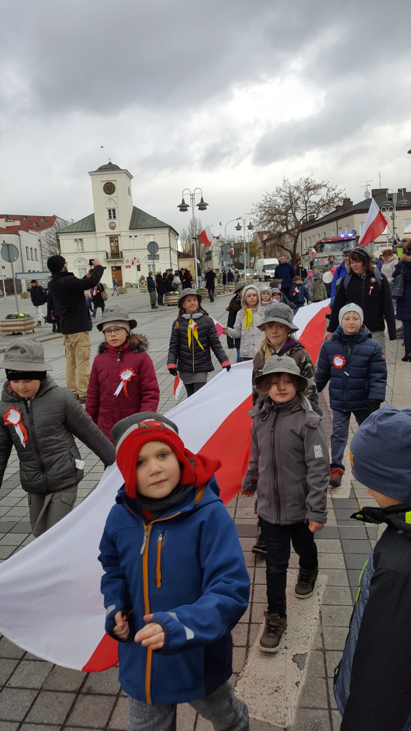 Przemarsz dzieci niosących flagę Polski na tle Urzędu stanu cywilnego